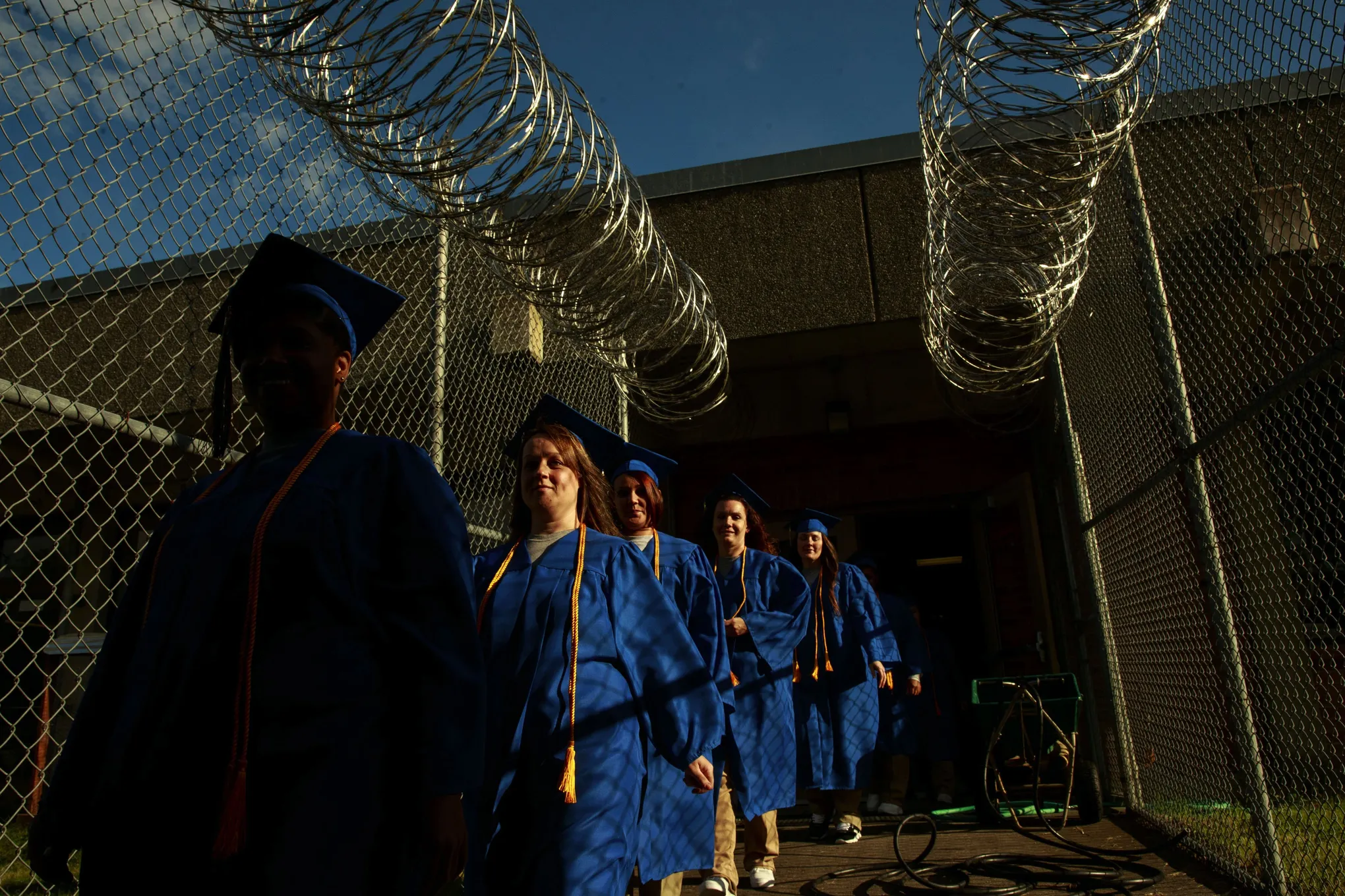 A photo shows female prisoners walking in front of fence dressed in blue graduate gowns.